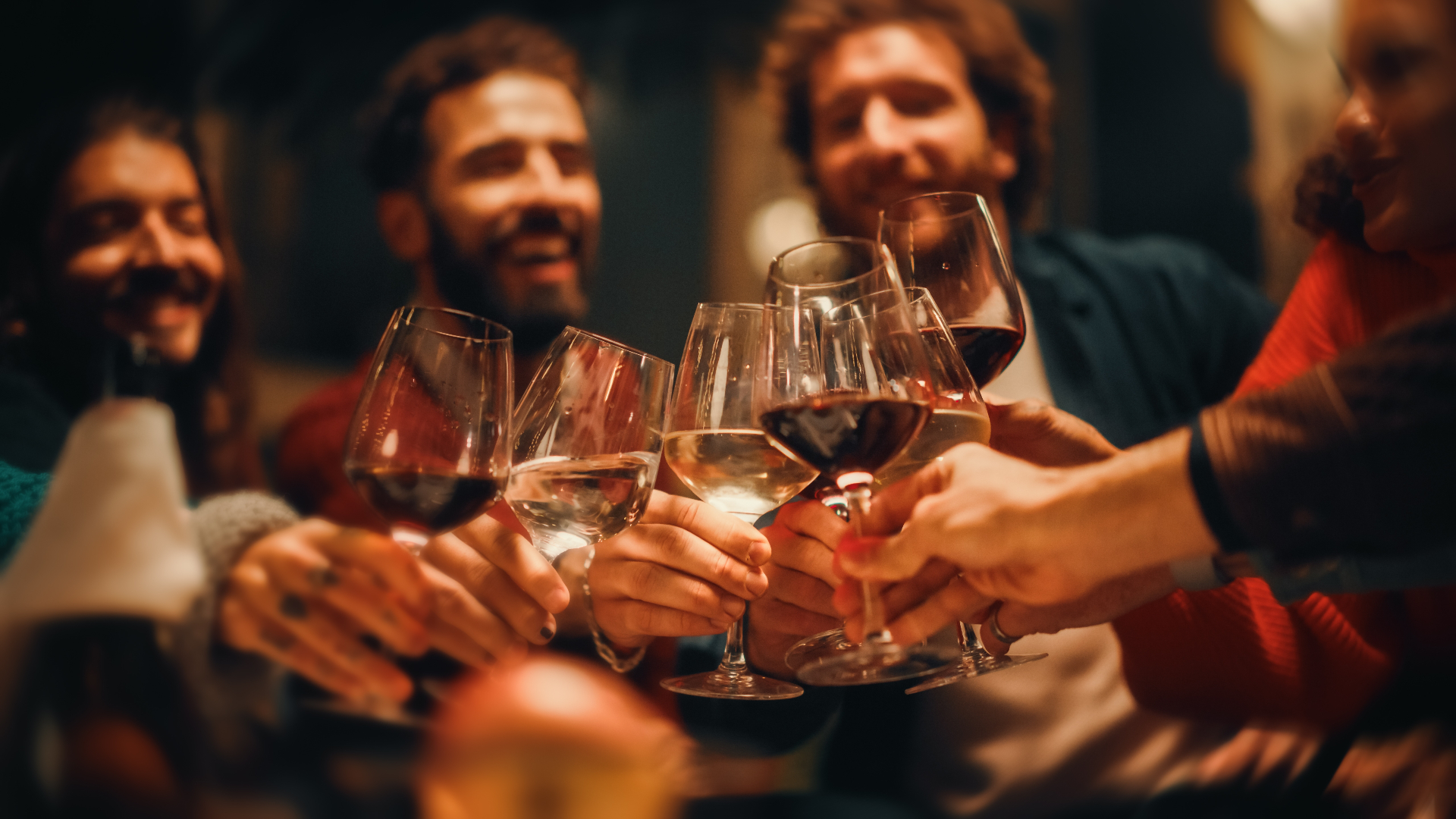 Friends raising glasses of red and white wine in a toast around a candlelit table.