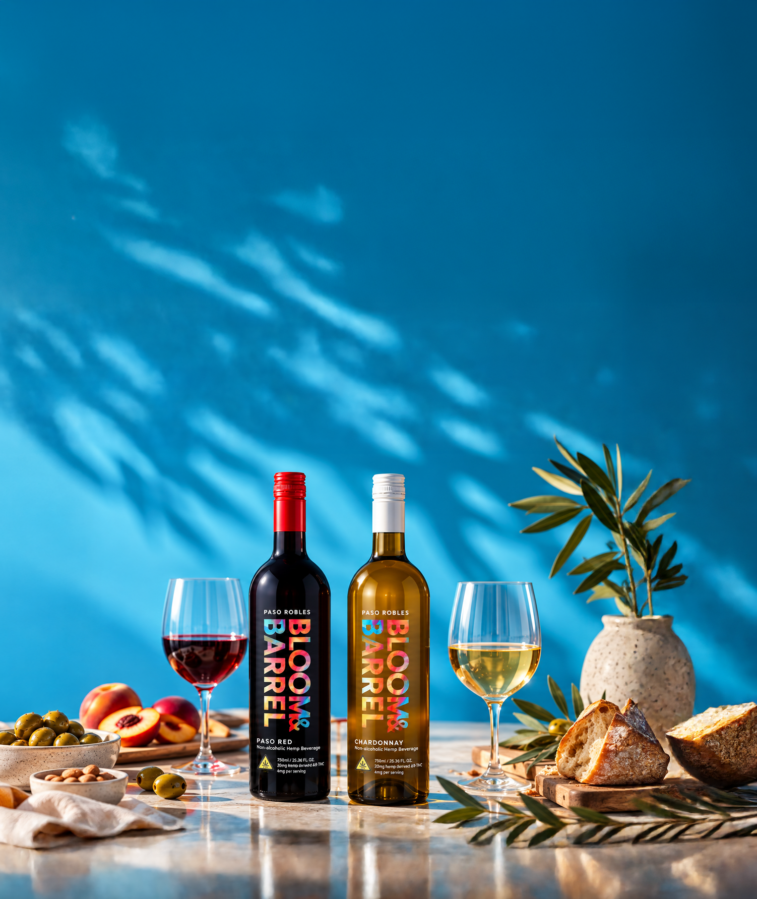 Bloom & Barrel Paso Red and Chardonnay bottles with poured glasses on a sunlit table against a blue wall